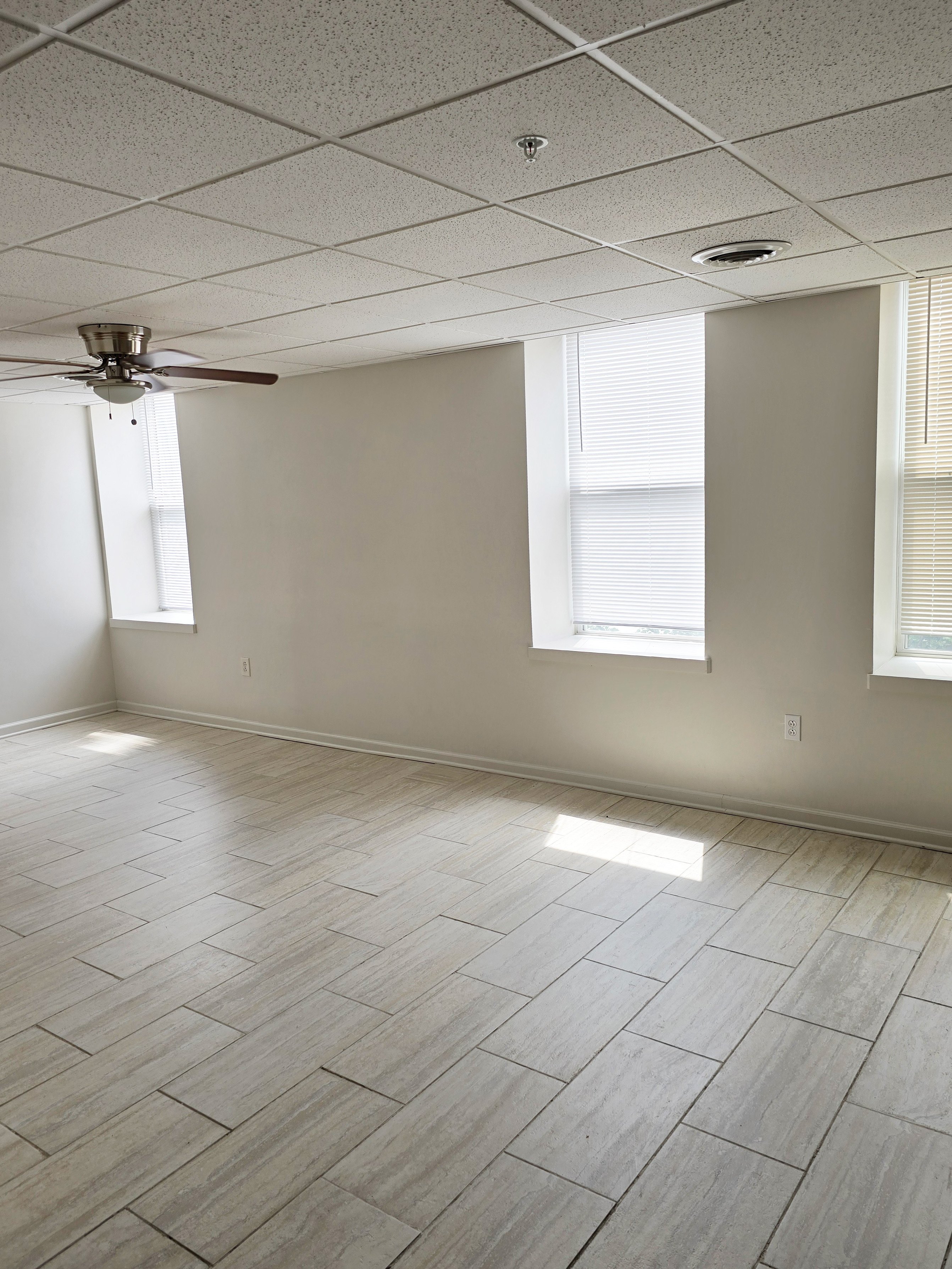 A room with a ceiling fan and light, tile flooring, and two windows.